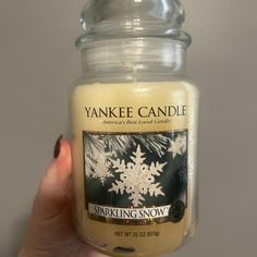 a hand holding a yankee candle with snowflakes on it