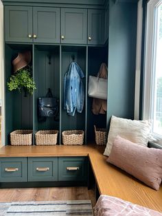 a mudroom with green cabinets and baskets on the floor, two coats hanging from hooks