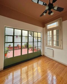 an empty room with wood flooring and green doors leading to a patio area that has a fan on the ceiling