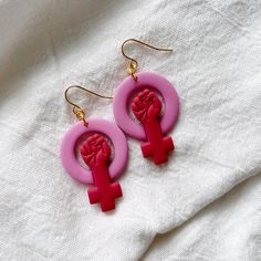 pink earrings with red symbols on them sitting on a white cloth covered surface, close - up