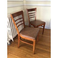 two wooden chairs sitting next to each other on a hard wood floor in front of a radiator