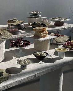 an assortment of desserts are displayed on white tables with bowls and plates in the middle