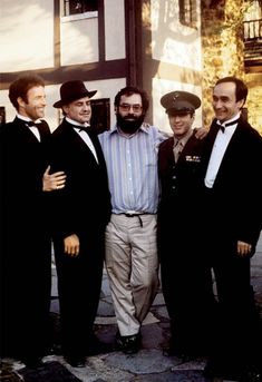 four men in tuxedos are posing for a photo outside an old - fashioned building