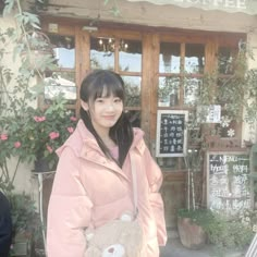 a woman standing in front of a coffee shop holding a teddy bear and smiling at the camera