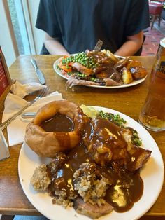 a man sitting at a table in front of two plates of food with meat and gravy