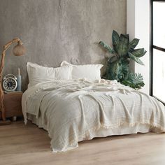 a bed with white linens and pillows in a bedroom next to a plant on the floor