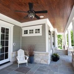 a white chair sitting on top of a patio under a wooden ceiling fan and windows