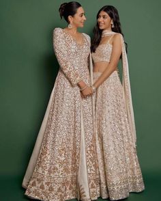 two women in matching outfits standing next to each other on a green background, one wearing a white and gold lehenga