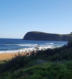 a beach with waves crashing on the shore and an island in the distance behind it