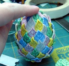 a person is holding an ornament made out of paper and plastic leaves on a table