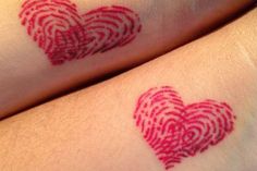 two people with tattoos on their arms that have red finger prints in the shape of hearts