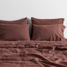 an unmade bed with red linens and pillows on it, in front of a white wall