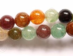 several different colored glass beads are lined up together on a white surface, with one bead in the middle