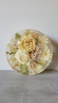 a glass plate with flowers on it sitting on a table next to a white wall