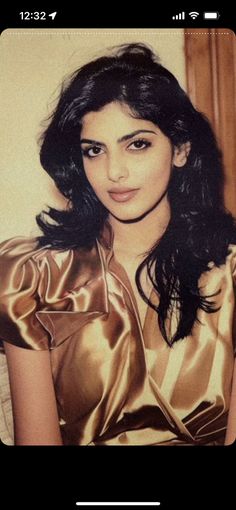 an old photo of a woman with long dark hair wearing a shiny gold dress and posing for the camera