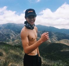 a shirtless man with no shirt on standing in front of mountains and trees wearing a bandana