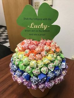 a potted plant filled with candy on top of a wooden table next to a sign that says, pick the lelipop with the lucky green dot on the bottom