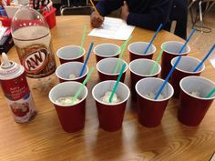 six red cups with blue straws on a table next to a person sitting at a desk