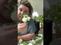 a woman sitting at a table with flowers in front of her and another person taking pictures