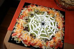 a spider web pizza on a black plate with cheese and tomato sauce in the center