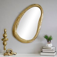 a mirror sitting on top of a white mantle next to a potted plant and books