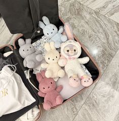 an open suitcase filled with stuffed animals on top of a marble floor next to a white bag