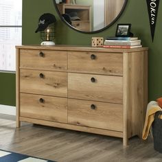 a wooden dresser sitting in front of a green wall with a round mirror above it