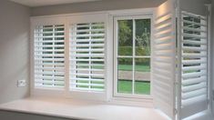 an empty room with white shutters on the windows and green grass in the background