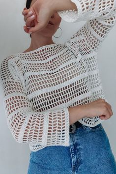 a woman is wearing a white sweater and blue jeans with her hands on her head