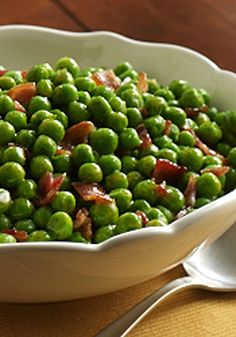 a white bowl filled with peas on top of a wooden table next to a fork