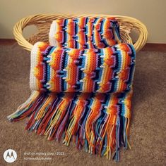 an orange and blue crocheted blanket sitting on top of a wicker chair