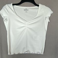 Hollister White Tee - Brand New Without Tags!! V-Neck Ruched Chest Lettuce Edge On Sleeve And Bottom Hem. Ribbed Detail Soft Material 88% Polyester / 12% Elastane Size: Xs Color: White Condition: Brand New!! Never Worn Or Washed. Casual Stretch V-neck Crop Top, Casual V-neck Stretch Crop Top, Casual White Stretch V-neck Top, Casual V-neck Fitted Top, Casual Fitted White V-neck Top, Casual White Fitted V-neck Top, Casual Fitted V-neck Top, White Fitted V-neck Top, White Fitted Top V-neck T-shirt