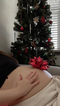 a pregnant woman laying in front of a christmas tree with her hand on her belly