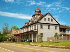 an old white building with a tower on top next to a road in front of some trees