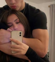 a man and woman hugging each other while looking at a cell phone screen in front of them