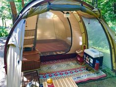 a tent is set up in the woods with picnic table and coolers on it