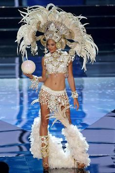 a model walks down the runway in an elaborate outfit with feathers and beads on her head