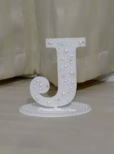 the letter j is made out of pearls and sits on top of a white bed