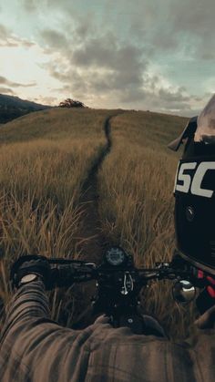 a person riding on the back of a motorcycle down a dirt road next to tall grass