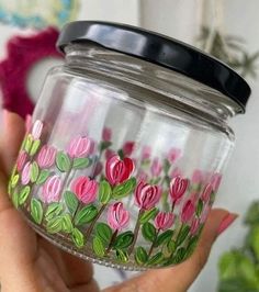 a hand holding a glass jar with flowers painted on it