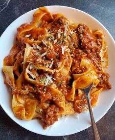 pasta with meat sauce and parmesan cheese on a white plate next to a fork