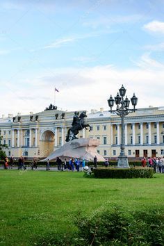 people are walking around in front of a large building with statues and lamps on it