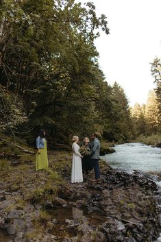 three people standing on rocks next to a river