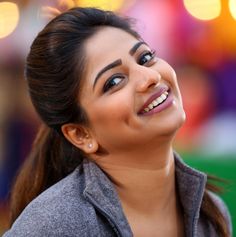 a woman smiling and looking up at the sky with bright lights in the back ground behind her