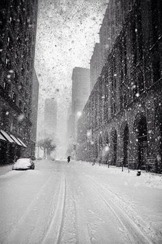 a person walking down a snow covered street in the middle of winter with tall buildings