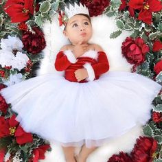 a baby dressed up in a white and red christmas outfit laying on top of flowers