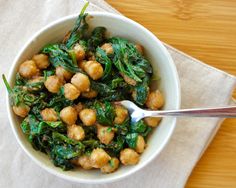 a white bowl filled with spinach and chickpeas on top of a wooden table