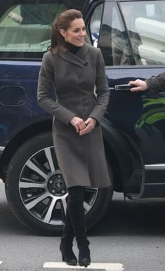 a woman in grey coat and black boots standing next to a car