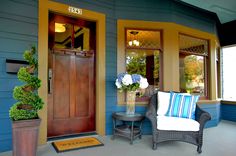 the front porch is decorated with blue and yellow accents, including two wicker chairs