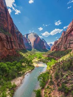 a river flowing through a lush green valley surrounded by red rocks and mountains under a blue sky with wispy clouds